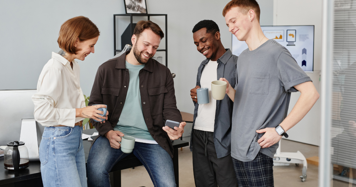 A group of people at work smiling and talking, representing collaboration and team engagement, reflecting the themes of presence and balance discussed in the blog.