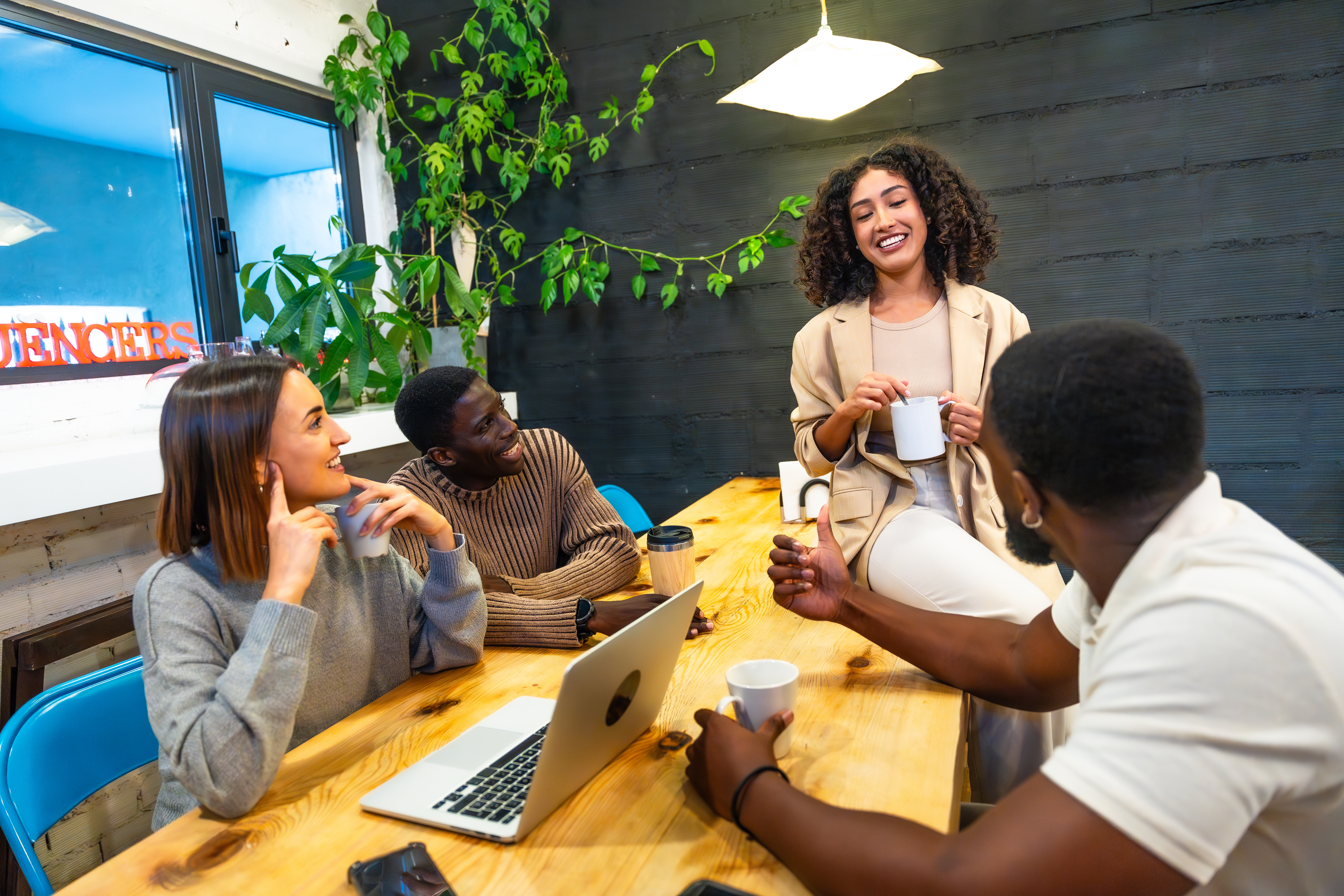 Featured image: A diverse group of coworkers chat and laugh around a wooden table during a coffee break in a modern coworking space, with laptops, mugs, and plants around them. - Read full post: What Does Belonging at Work Really Mean?