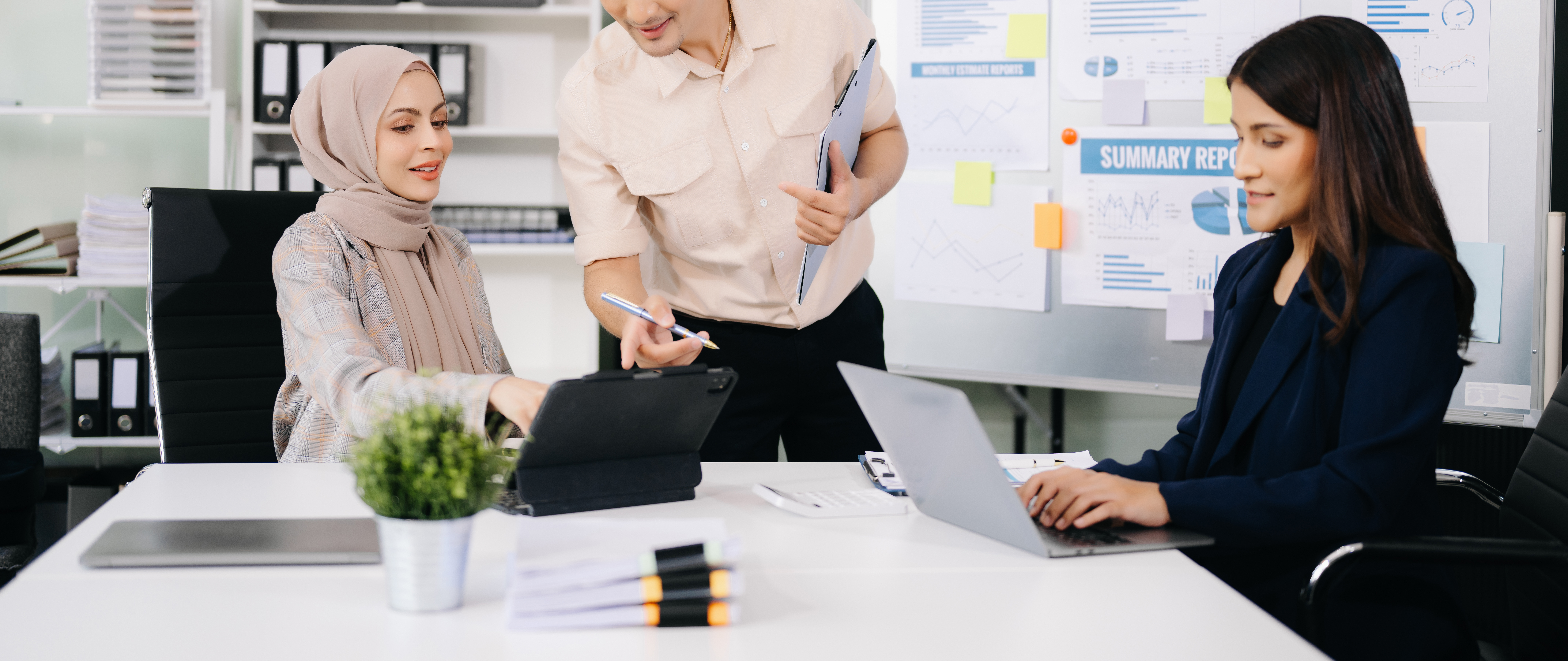 Featured image: Three colleagues collaborating at a desk in an office, reviewing information on a tablet and laptop, with charts and reports displayed on a board in the background. - Read full post: What Is Emotional Safety at Work and Why It Matters for Team Performance