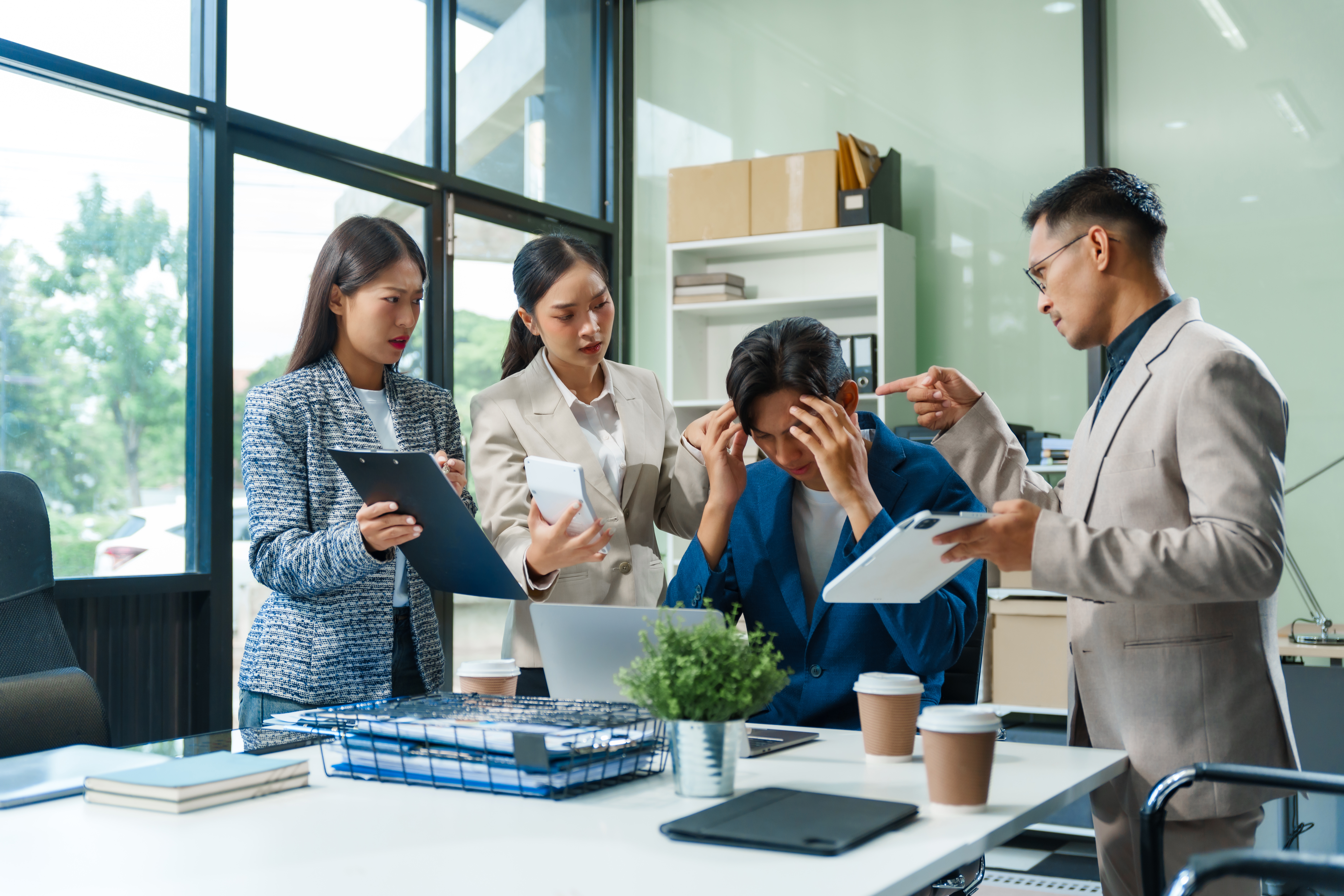 Featured image: A stressed office worker sits at a desk holding their head while colleagues stand around reviewing documents and tablets in a busy modern workplace. - Read full post: When Work Feels Heavier Than It Should: Understanding Emotional Safety