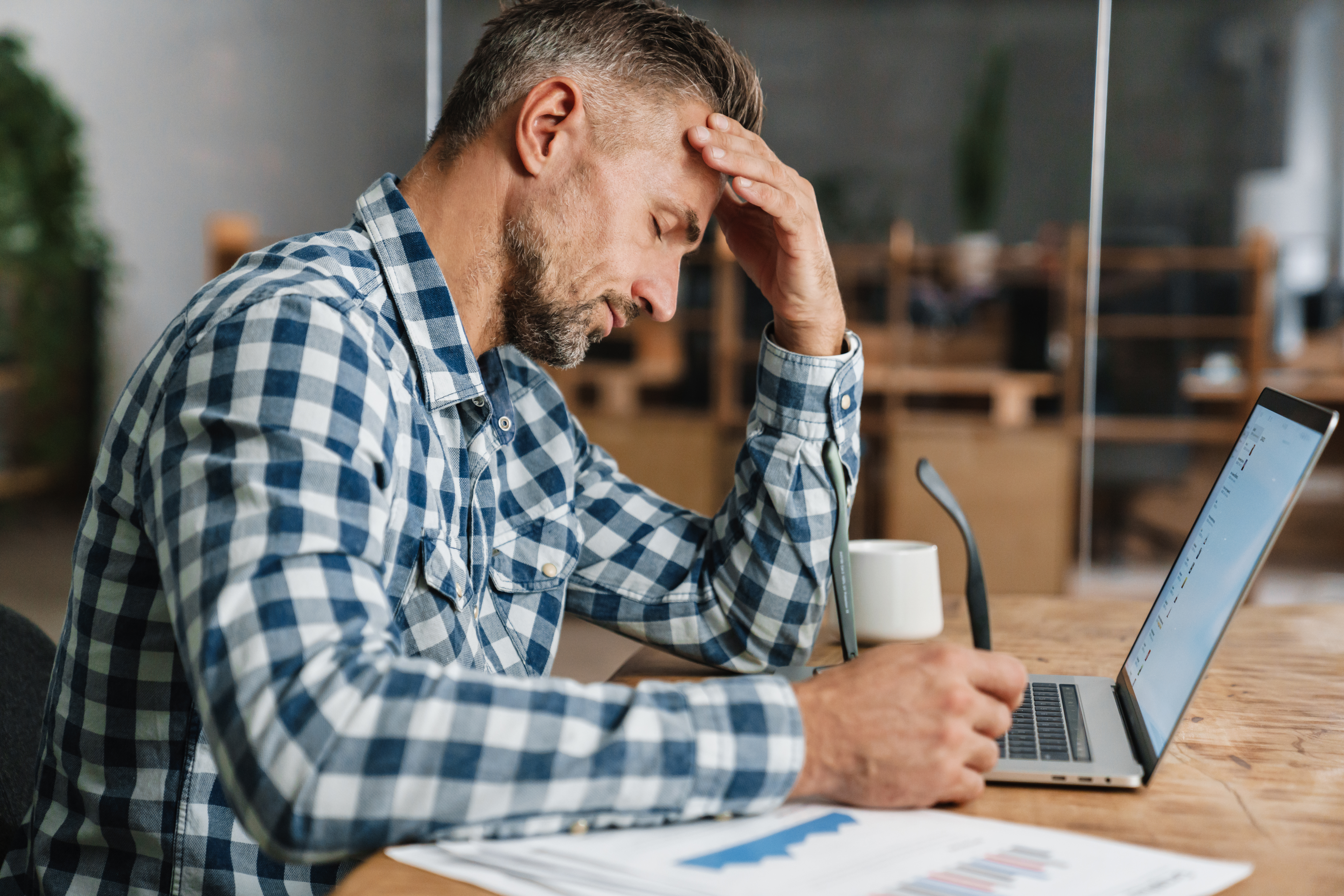 Featured image: A tired man working at a desk, resting his head in one hand while looking at a laptop, with papers and a coffee mug nearby, conveying stress or mental fatigue at work. - Read full post: Men’s Mental Health at Work